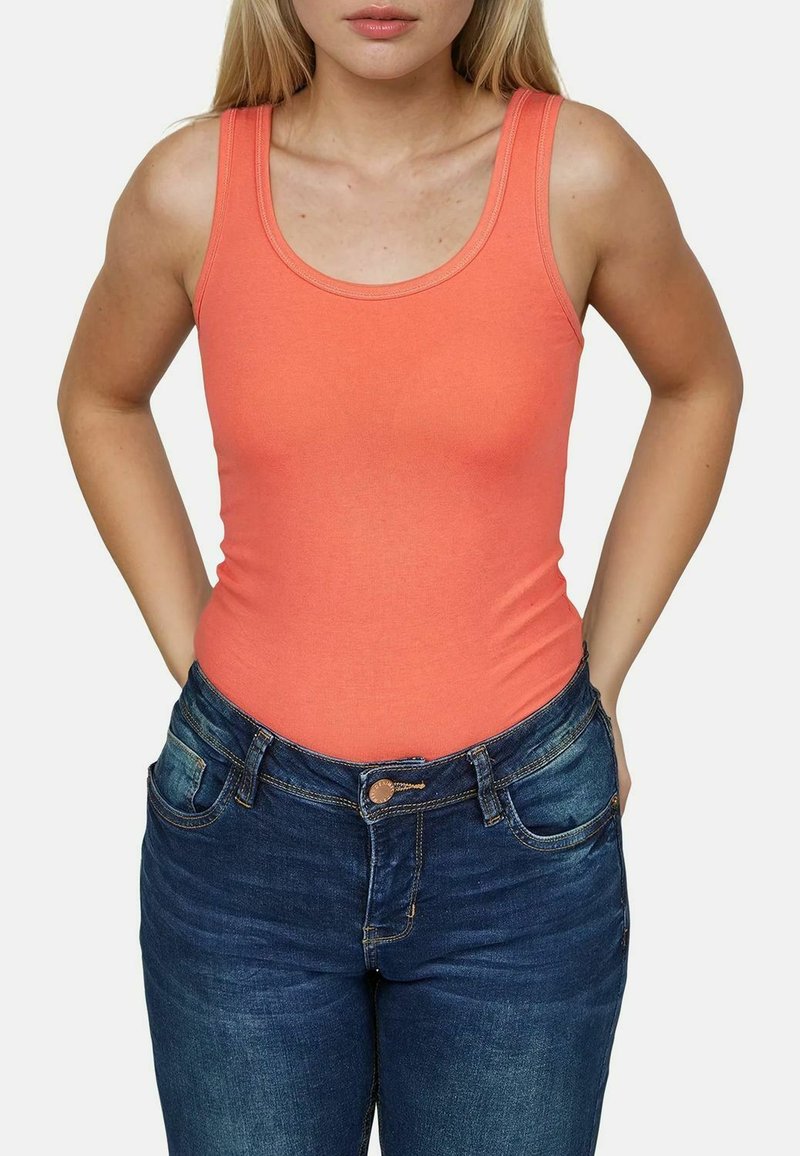 Koraalkleurige tanktop met brede banden, getailleerd ontwerp. Draagt met donkerblauwe denimjeans met voorkezen en een knoopsluiting.