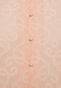 Blusa rosa chiaro con un motivo floreale testurizzato, caratterizzata da bottoni di tessuto tondi e una leggera piegatura nel materiale.