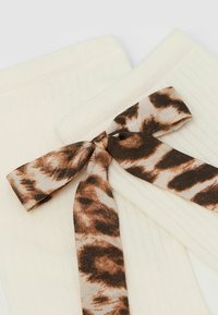 Chaussettes côtelées de couleur crème avec un ruban imprimé léopard marron noué en forme de nœud en haut. Texture douce et design structuré.