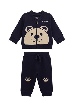 Survêtement marin pour tout-petits avec un visage d'ours sur la veste zippée et des empreintes de pattes beiges sur le pantalon, avec le logo "GUESS" sur la poitrine.