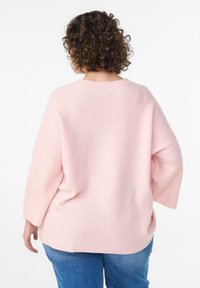 Light pink oversized knitted sweater with a ribbed texture, dropped shoulders, and a wide neckline, paired with blue jeans.