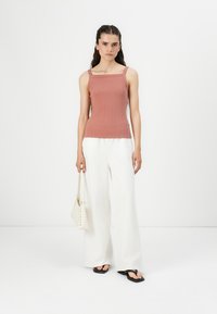 Ljust rosa ribbad linne med fyrkantig halsringning, parat med lösa vita byxor och svartaFlip-flops, accessoriserat med en vit väska.