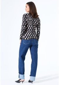 Zwarte lange mouwen top met een licht crèmekleurig ikatpatroon, gecombineerd met blauwe denim jeans met opgerolde mouwen en zwarte hoge hakken.