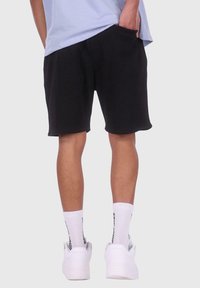 Sorte shorts lavet af tekstureret stof med en afslappet pasform, der har sidelommer og en elastisk talje, parret med hvide sneakers og sokker.