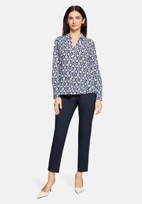 Chemisier à manches longues à motifs bleus et blancs avec un col, associé à un pantalon bleu marine et des talons crème.