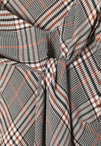 Tissu à carreaux noir, blanc et marron noué en un nœud, montrant un motif tissé détaillé et une texture.