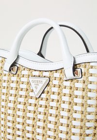 Borsa tote intrecciata in tonalità tan e bianca, con un logo triangolare argento e manici in pelle bianca. I dettagli del tessuto testurizzato sono ben evidenti.