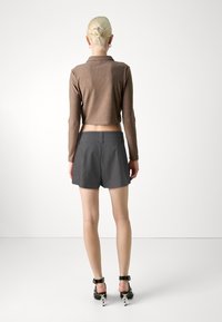 Hnědý proužkovaný krátký top a šedé kostkované tailored šortky, které ukazují přiléhavý design a plochý pás. Černé sandály na podpatku dotvářejí celkový vzhled.