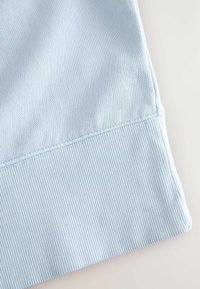 Helles blaues Baumwollgewebe mit geripptem Muster und einem Saum, der eine fein genähte Naht aufweist, wodurch eine glatte, weiche Oberfläche entsteht.