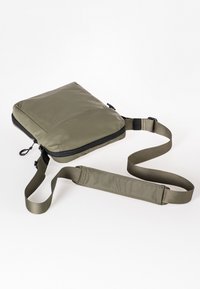Olijfgroene schoudertas met een gladde, gewatteerde ontwerp, voorzien van een zwarte rits en een verstelbare band voor comfortabel dragen.