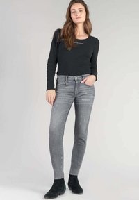Haut noir à manches longues avec texture côtelée, associé à un jean slim délavé gris et des bottines noires à motif subtil.