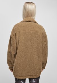 Brun fleecejakke med en strukturert overflate, oversized passform, krage og lange ermer, med en rett hem bak.
