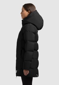 Anorak negro con capucha, con diseño acolchado, textura suave y cremallera lateral. La longitud llega hasta la mitad del muslo.