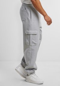 Grå byxor i sweatpantsmodell med elastisk midja och muddar, med två sidofickor med lock och en slät yta.