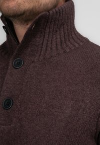 Suéter marrón de punto con un alto cuello acanalado, presenta un cierre con cremallera y dos botones negros en la parte delantera. Textura suave, material cálido.