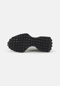 Semelle extérieure en caoutchouc noir avec des rainures circulaires texturées, milieu de semelle blanc incurvé, avec un accent vert sur le talon. Matériaux lisses dans l'ensemble.