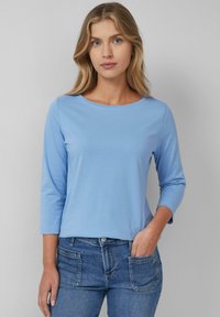 Light blue long-sleeve top with a round neckline, made of soft fabric. Styled with jeans featuring front pockets and a classic fit.