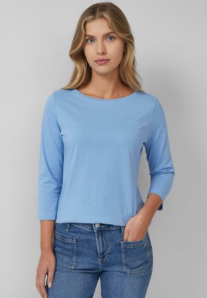 Lichtblauw lang shirt met een ronde halslijn, gemaakt van zachte stof. Gestyleerd met jeans met voorzakken en een klassieke pasvorm.