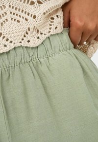 Lichtgroene rok met een elastische tailleband, gemaakt van zachte, gestructureerde stof. Een crèmekleurig gebreid topje bedekt een deel van de tailleband.