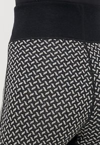 Höga leggings i svart och vitt hundtandsmönster, tillverkade av ett texturerat stickat tyg med ett smidigt midjeband och sömdetaljer.