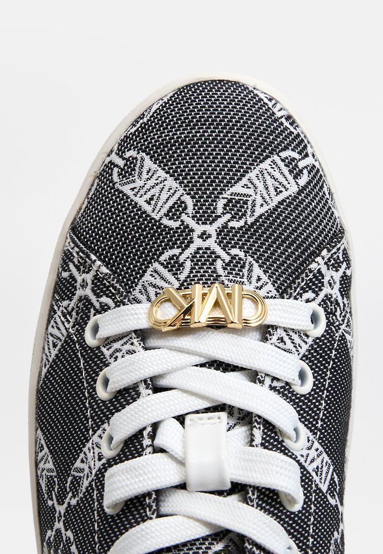 Baskets en toile noires et blanches à motif avec des lacets blancs et un accent logo doré sur la languette. Tige en textile texturé.