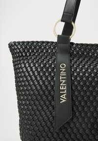 Black woven handbag featuring a textured surface, a leather strap, and a gold-tone circular hardware detail. "VALENTINO" embossed on the strap.