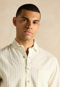 Heled värvi triibuline nupuga särk, millel on pehme tekstuur, terav krae ja rinna tasku koos kerge brändimisega.