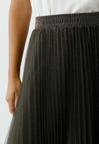Black pleated skirt with a shimmering texture, elastic waist, and layered tulle fabric. The pleats create a flowy silhouette.