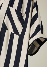 Camisa de manga corta a rayas en azul marino y crema con un bolsillo en el pecho y un corte relajado. Fabricada con un tejido texturizado y un acabado suave.