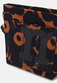 Suorakulmainen kangaspussi tummansinisellä ja oranssilla kukkakuviolla, etupuskurissa iso harmaa "m" ja "marimekko" -teksti.