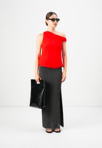 Mujer con gafas de sol negras, top rojo de un solo hombro, falda larga oscura con abertura lateral, llevando un bolso tote negro y usando tacones abiertos.