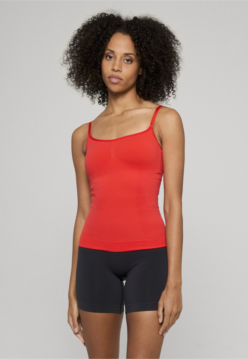 Rød tettsittende tanktop med tynne stropper, sømløst design og elastisk stoff, kombinert med svarte shorts til midten av låret med glatt tekstur.