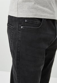 Black denim jeans with a straight cut, featuring front and back pockets, metal buttons, and a soft texture.