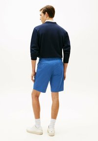 Sudadera marina y pantalones cortos azules de algodón; los pantalones cortos cuentan con bolsillos traseros con botones; se llevan con zapatillas blancas y calcetines cortos.