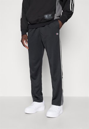 Black and gray athletic pants with white side stripes, made of a smooth material. Features a small logo on the thigh and a relaxed fit.