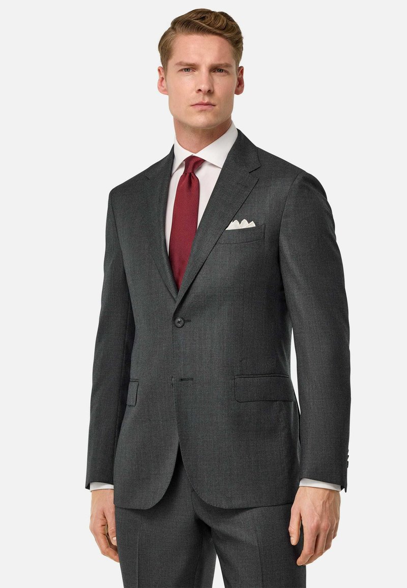 Veste de costume gris charcoal avec un revers cranté, deux poches avant et une fermeture à un bouton. Associée à une cravate bordeaux et un mouchoir de poche blanc.