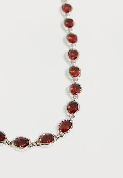 Ogrlica z ovalnimi globoko rdečimi dragimi kamni, vgrajenimi v srebrni metal, razporejenimi v neprekinjen vzorec povezav na belem ozadju.