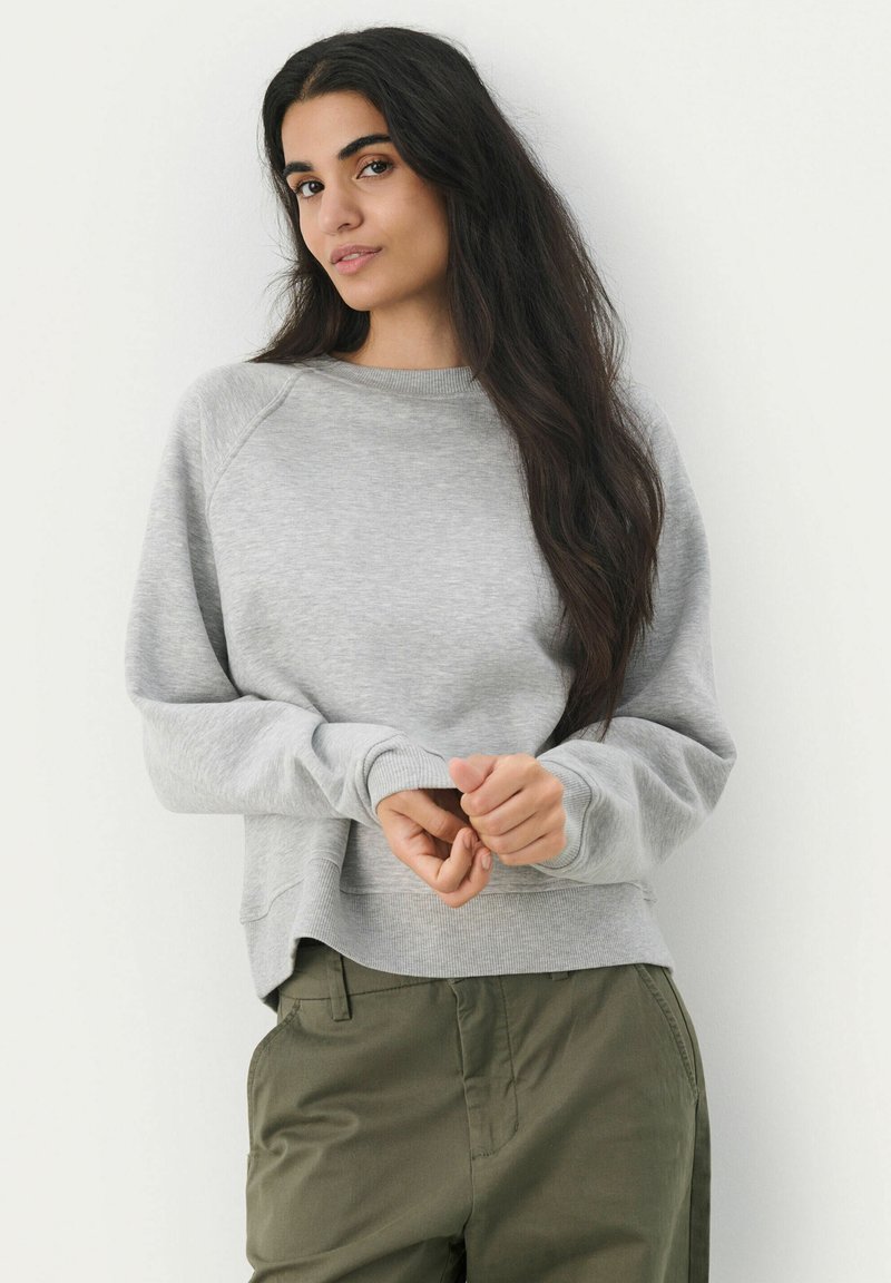 Grau Sweatshirt mit lockerer Passform, gerippten Bündchen und Bund. Weiche Textur, lange Ärmel und Raglan-Design. Getragen mit olivgrünen Hosen.