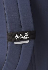 Tengerészkék szövet, sima textúrával, fekete címkével, rajta a "Jack Wolfskin" felirattal és egy mancsikonnal. Az él mentén varrás részletek.