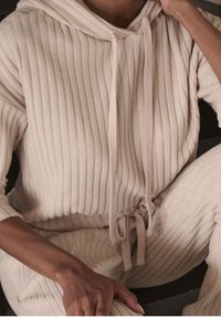 Jasno beżowy, prążkowany hoodie z sznurkiem, w komplecie z pasującymi prążkowanymi spodniami. Posiada teksturowany materiał i luźny krój.