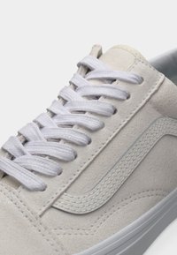 Κοντινή όψη μπεζ σουέντ αθλητικού παπουτσιού με λευκά κορδόνια και χαρακτηριστική ρίγα στο πλάι, σε λευκό φόντο.