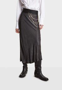Jupe noire longue jusqu'à la cheville en matériau lisse, avec une large ceinture et un embellissement en chaînes argentées superposées au niveau des hanches.