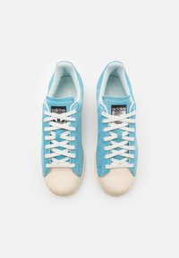 Ljusblå mockaskor med vita snören och gummitå. Har en svart logopatch på plösen och mjuk foder för komfort.