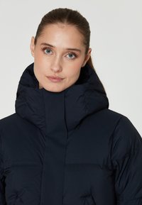 Chaqueta acolchada azul marino con un alto cuello y capucha. Diseño texturizado y acolchado con un acabado suave y cremallera oculta.