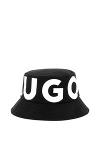 Chapeau seau en coton noir avec un large bord, portant de grandes lettres blanches épelant "HUGO" autour de la bande. Texture lisse et forme structurée.