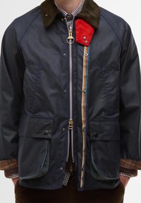 Ναυτικό αδιάβροχο μπουφάν με κολάρο από χοντρή υφασμάτινη ύλη, κόκκινο λογότυπο, λεπτομέρειες με ουράνιο τόξο και δύο μπροστινές τσέπες. Μεταλλικό φερμουάρ και κλείσιμο με κουμπιά.