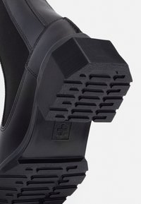 Svart glidsko med en texturerad gummisula, hexagonala former och greppmönster. Slät ovandel med elastiska sidopaneler.