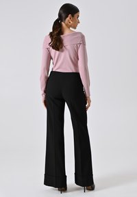 Maglione rosa scollato sulle spalle abbinato a pantaloni neri a vita alta. Tessuto texturizzato, design a gamba larga e vestibilità su misura con orlo svasato.