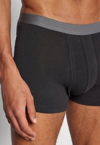 Schwarze Baumwoll-Boxershorts mit einem grauen elastischen Bund, die eine glatte Textur und einen enganliegenden Schnitt aufweisen, akzentuiert durch tonale Nähte.