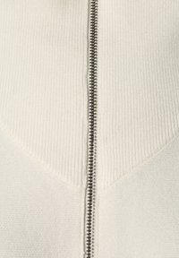 Gros plan d'un tissu blanc côtelé avec une fermeture éclair argentée courant verticalement au centre.